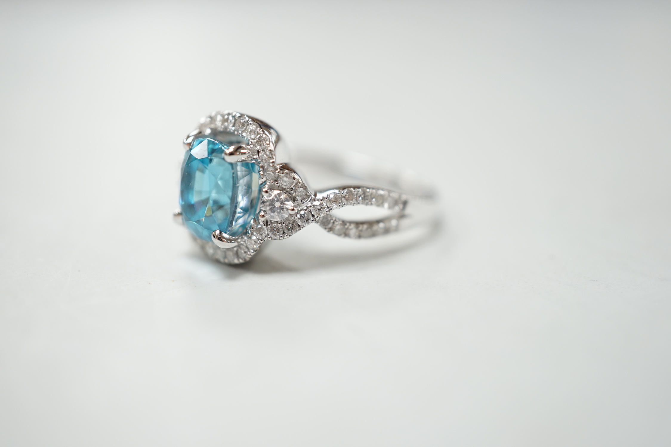 A modern 14k white metal, cushion cut blue zircon and diamond chip set cluster dress ring, with diamond chip set shoulders, size O, gross weight 6.8 grams.